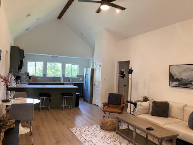 living room featuring ceiling fan, high vaulted ceiling, sink, beam ceiling, and light hardwood / wood-style flooring