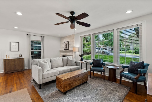 living room with ceiling fan, a stone fireplace, and dark wood-type flooring