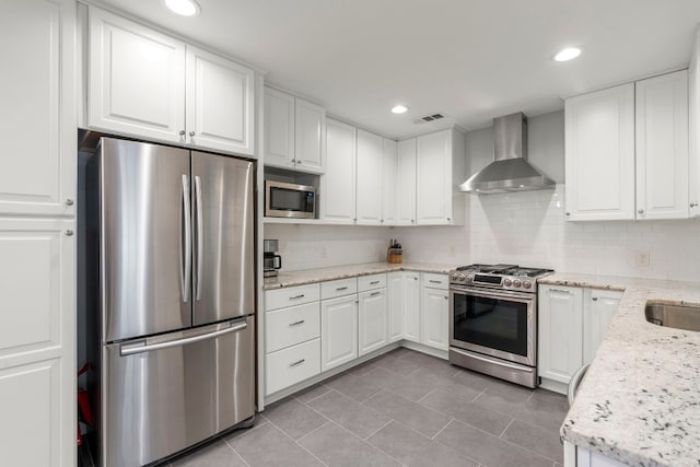 kitchen with decorative backsplash, appliances with stainless steel finishes, light stone counters, wall chimney exhaust hood, and white cabinets