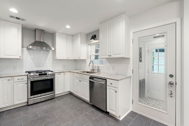 kitchen featuring white cabinets, wall chimney range hood, sink, light stone countertops, and appliances with stainless steel finishes