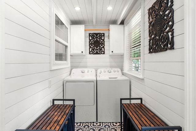 washroom with washing machine and dryer, wooden walls, and cabinets