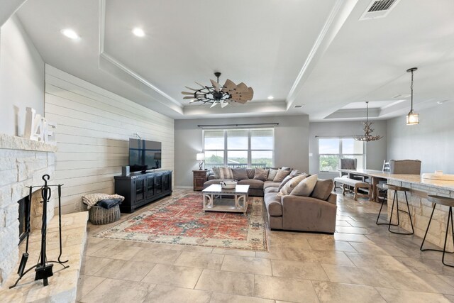 living room featuring light tile patterned flooring, a fireplace, ceiling fan with notable chandelier, and a raised ceiling