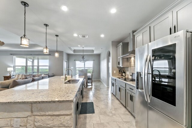 kitchen with stainless steel fridge with ice dispenser, wall chimney range hood, backsplash, sink, and a center island with sink