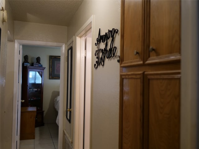 hallway with a textured ceiling and light tile patterned floors