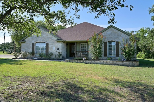 view of front of home with a shingled roof, a front yard, and stone siding