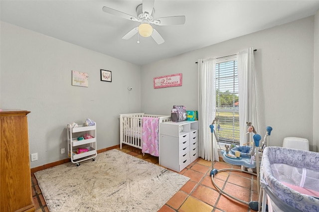 bedroom featuring a nursery area, a ceiling fan, and baseboards