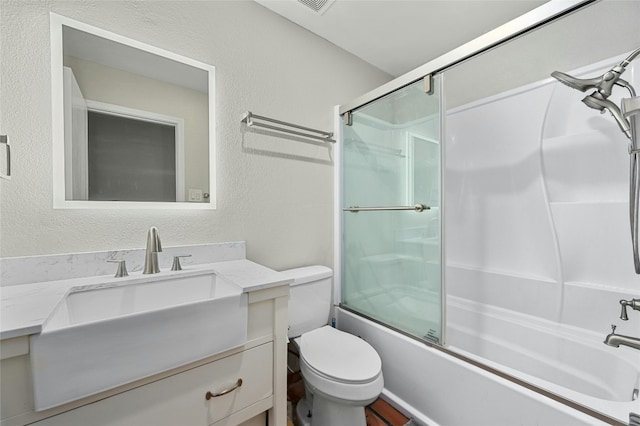 bathroom featuring a textured wall, shower / bath combination with glass door, vanity, and toilet