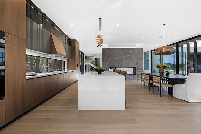 kitchen with a kitchen island, a fireplace, decorative light fixtures, dark brown cabinetry, and light hardwood / wood-style flooring