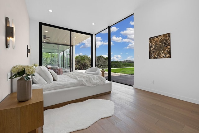 bedroom with access to exterior, expansive windows, a sunroom, wood finished floors, and baseboards