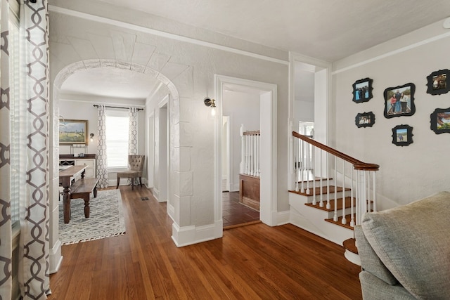 hall with arched walkways, dark wood finished floors, stairway, and baseboards