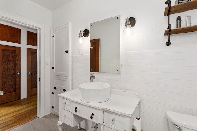 bathroom featuring a wainscoted wall, tile walls, toilet, vanity, and wood finished floors