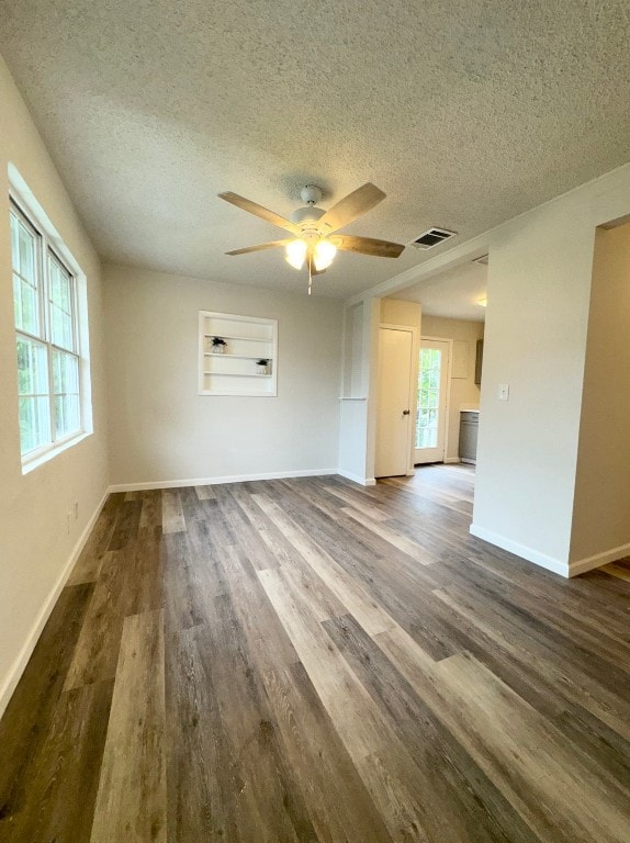 empty room with a textured ceiling, dark hardwood / wood-style flooring, and a healthy amount of sunlight