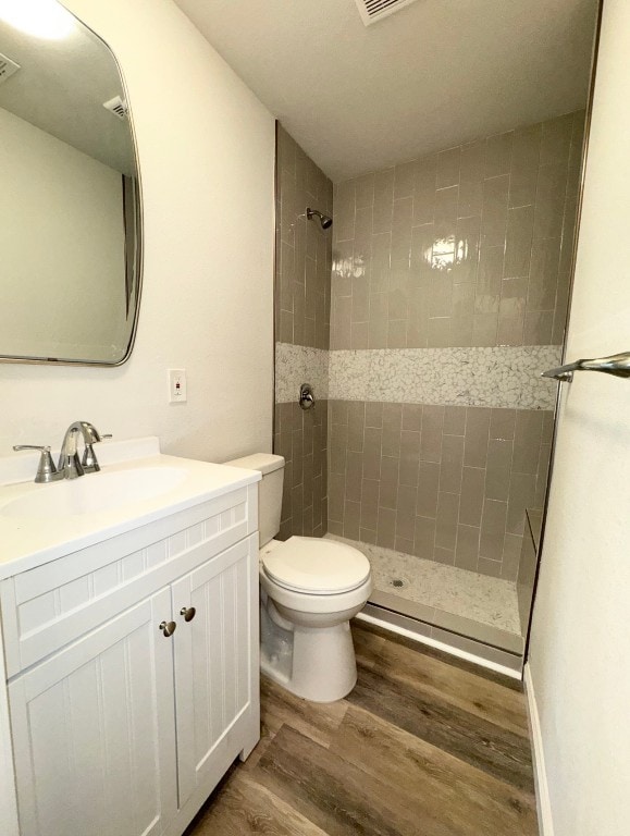 bathroom featuring hardwood / wood-style flooring, vanity, toilet, and tiled shower