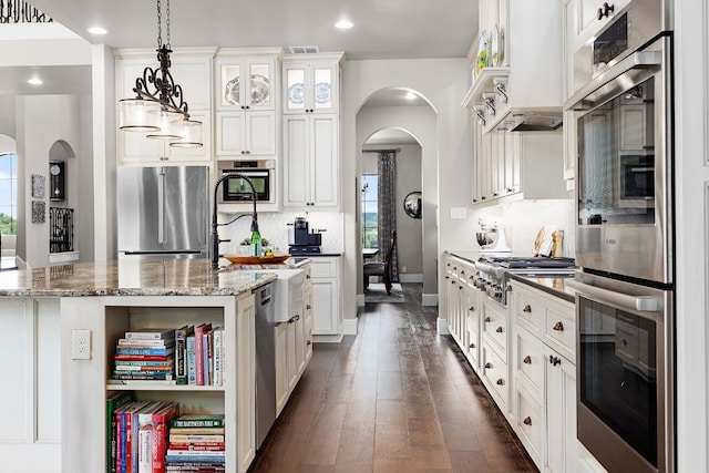 kitchen with appliances with stainless steel finishes, dark hardwood / wood-style flooring, white cabinetry, and dark stone counters