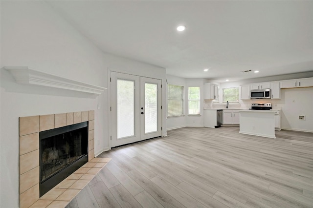 unfurnished living room featuring light wood-type flooring, sink, a tile fireplace, and french doors