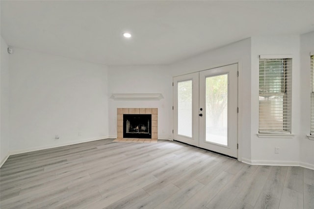 unfurnished living room featuring french doors, light hardwood / wood-style floors, and a tiled fireplace