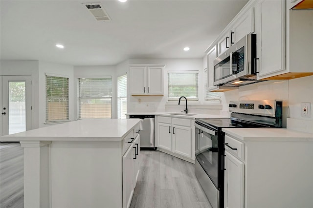 kitchen featuring appliances with stainless steel finishes, a center island, light hardwood / wood-style flooring, and white cabinetry