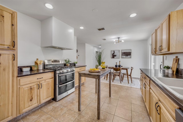 kitchen with sink, light tile patterned floors, range with two ovens, wall chimney exhaust hood, and light brown cabinets