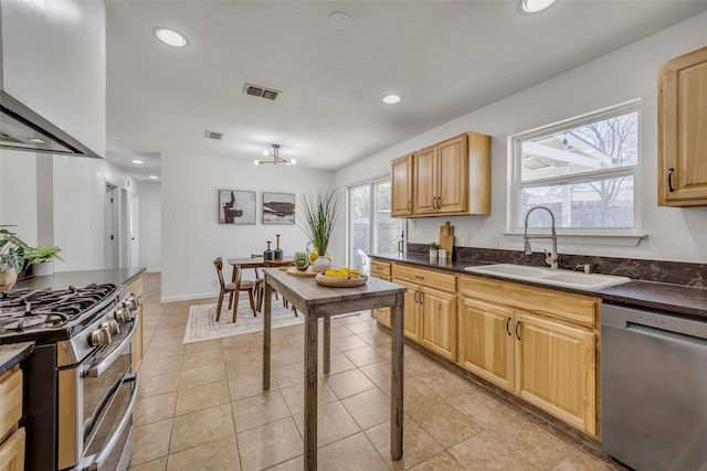 kitchen with light tile patterned flooring, appliances with stainless steel finishes, light brown cabinetry, sink, and wall chimney exhaust hood