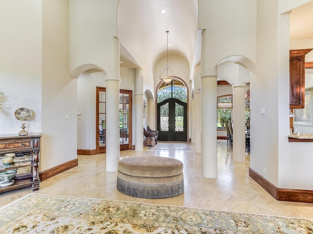 entrance foyer featuring french doors, a towering ceiling, and ornate columns