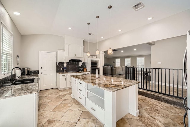 kitchen featuring visible vents, a sink, a center island, white cabinetry, and light stone countertops