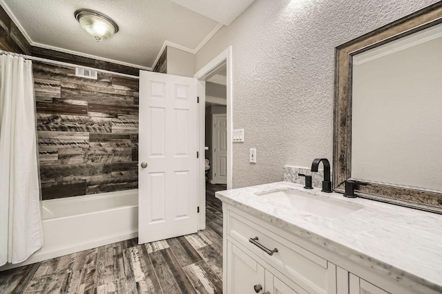 bathroom featuring vanity, wood finished floors, shower / bath combination with curtain, crown molding, and a textured wall