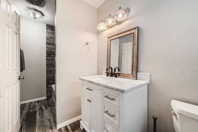 bathroom with toilet, wood finished floors, vanity, and a textured wall