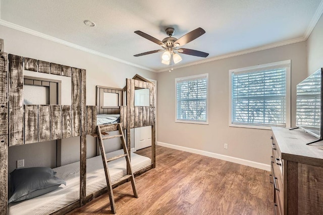 bedroom featuring a textured ceiling, wood finished floors, crown molding, baseboards, and ceiling fan