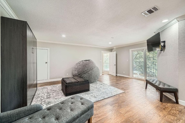 living area with visible vents, baseboards, ornamental molding, wood finished floors, and a textured ceiling