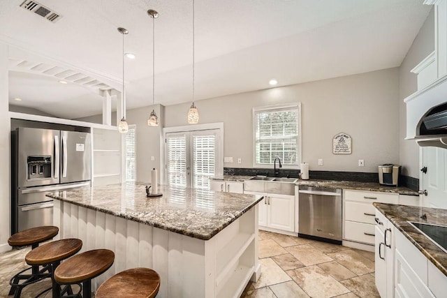 kitchen with visible vents, dark stone counters, a kitchen breakfast bar, white cabinets, and stainless steel appliances