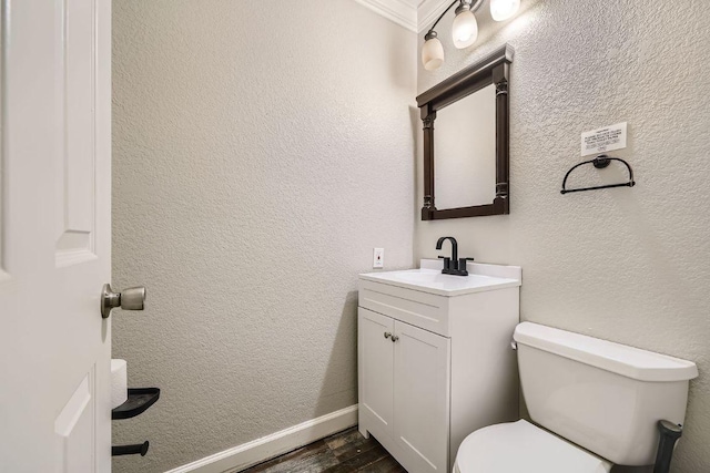 half bathroom with vanity, wood finished floors, toilet, and a textured wall