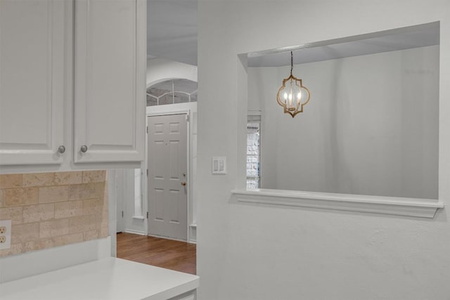 interior space featuring a chandelier, wood-type flooring, white cabinetry, and hanging light fixtures