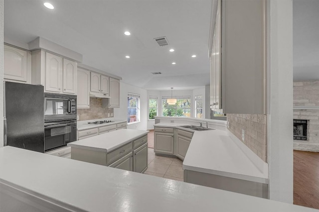 kitchen featuring light wood-type flooring, sink, black appliances, a fireplace, and a kitchen island