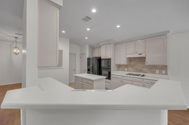 kitchen featuring black appliances, light wood-type flooring, tasteful backsplash, decorative light fixtures, and kitchen peninsula