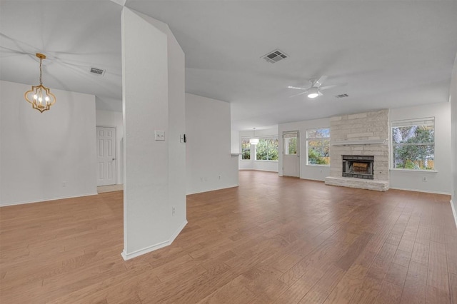 unfurnished living room featuring a stone fireplace, a healthy amount of sunlight, ceiling fan with notable chandelier, and light hardwood / wood-style floors