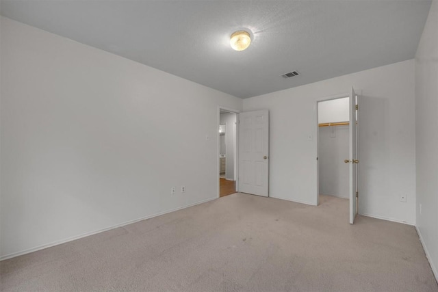 unfurnished bedroom with a spacious closet, light carpet, and a closet