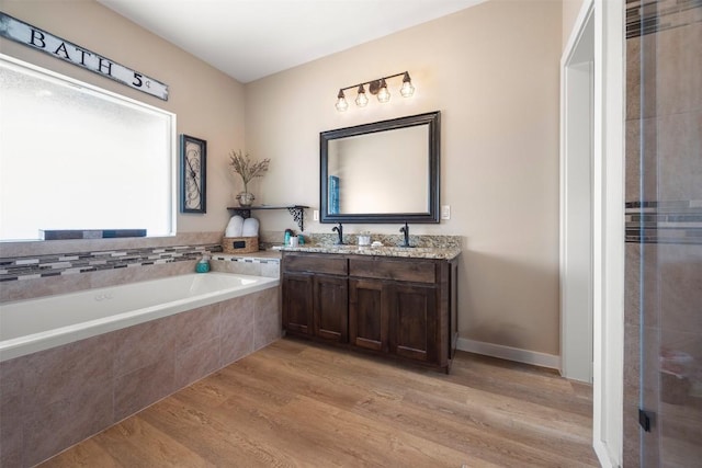 bathroom with a garden tub, double vanity, and wood finished floors