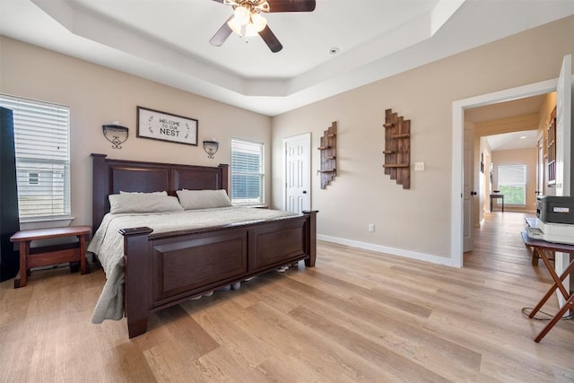 bedroom featuring light wood finished floors, baseboards, a tray ceiling, and ceiling fan