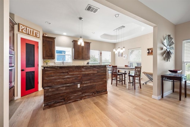 kitchen featuring a raised ceiling, visible vents, hanging light fixtures, light wood-style flooring, and light stone countertops