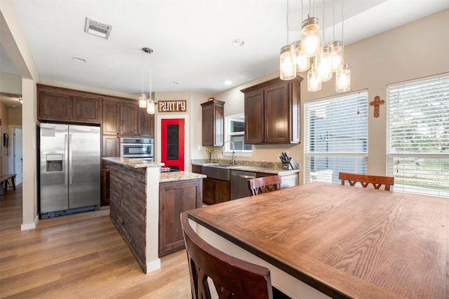 kitchen with dark brown cabinetry, visible vents, appliances with stainless steel finishes, a center island, and decorative light fixtures