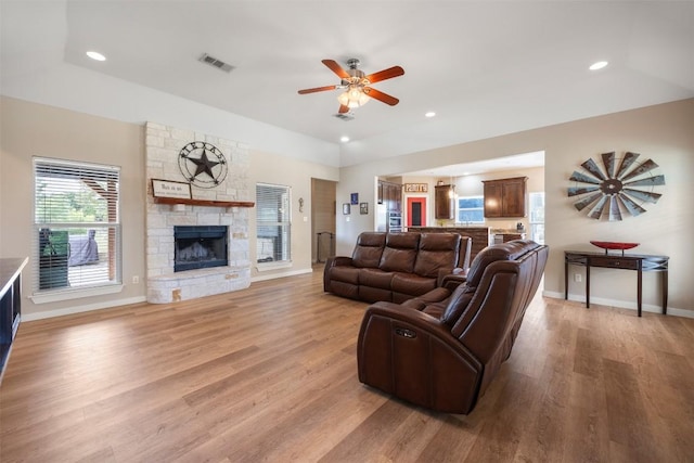 living room with baseboards, visible vents, a stone fireplace, and light wood finished floors