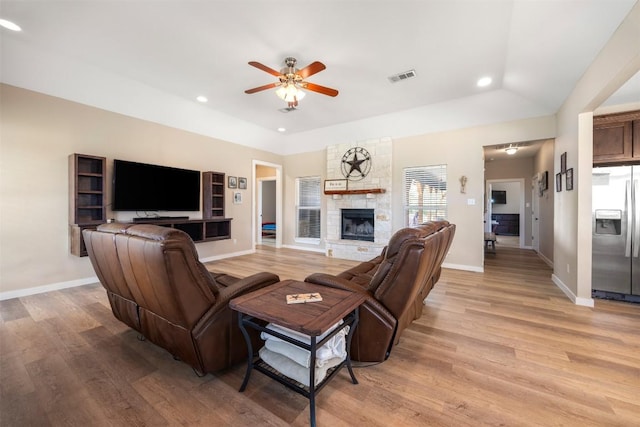 living room featuring visible vents, light wood-style floors, a ceiling fan, a stone fireplace, and baseboards