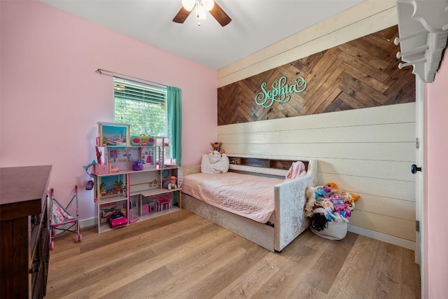 bedroom featuring wood walls, ceiling fan, baseboards, and wood finished floors