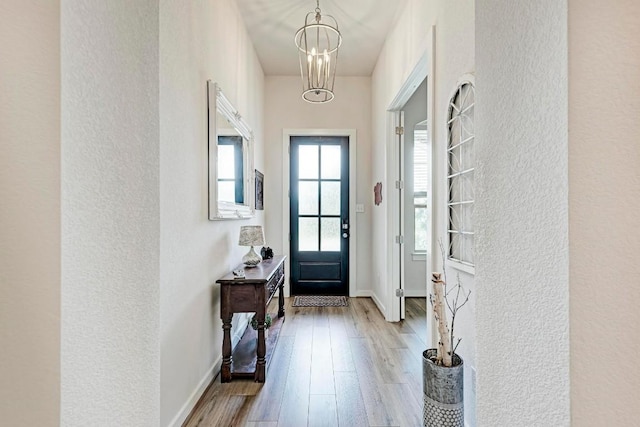 doorway with a notable chandelier, baseboards, and wood finished floors