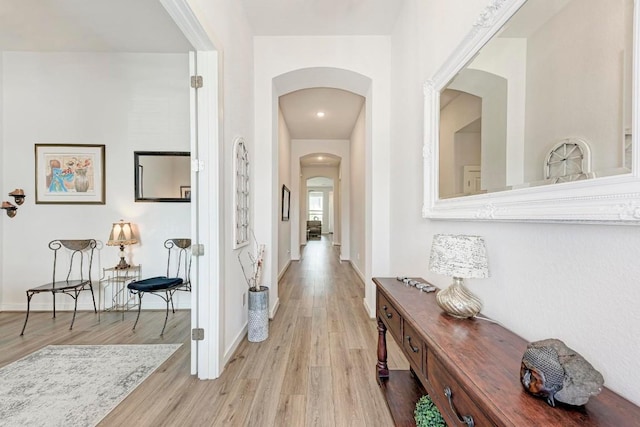 hall featuring arched walkways, baseboards, and light wood-style floors