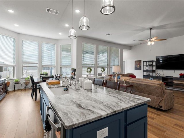 kitchen with visible vents, light wood-style flooring, stainless steel dishwasher, a sink, and light stone countertops