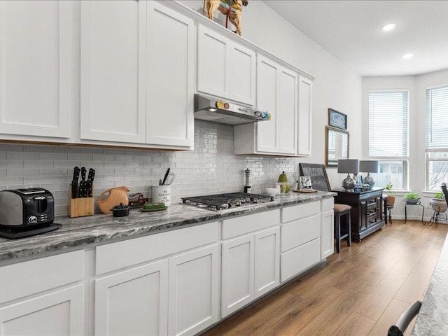 kitchen with stainless steel gas cooktop, backsplash, white cabinets, wood finished floors, and under cabinet range hood