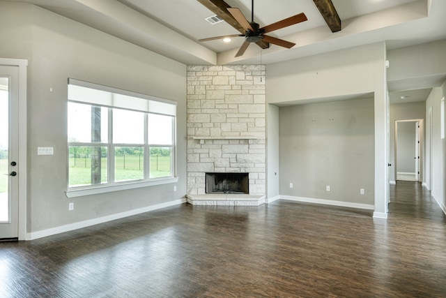 unfurnished living room featuring beamed ceiling, ceiling fan, a stone fireplace, and dark wood-type flooring