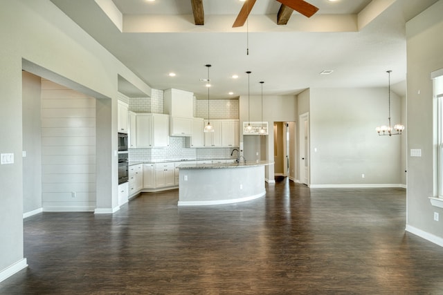 kitchen featuring decorative light fixtures, oven, white cabinets, backsplash, and a center island with sink