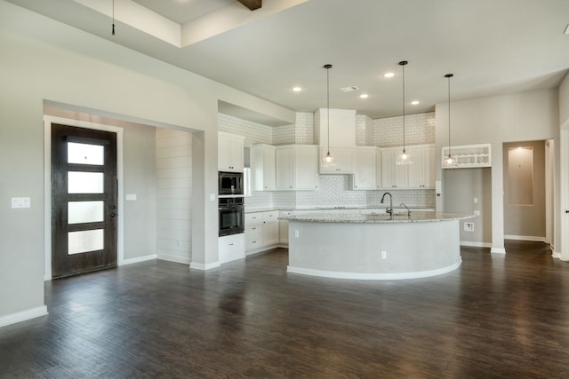 kitchen with built in microwave, white cabinetry, a center island with sink, and black oven